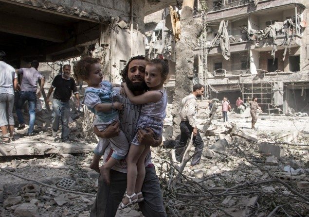 Un hombre sirio lleva a sus dos niñas mientras camina a través de los escombros. (Karam al-Masri / AFP / Getty Images)