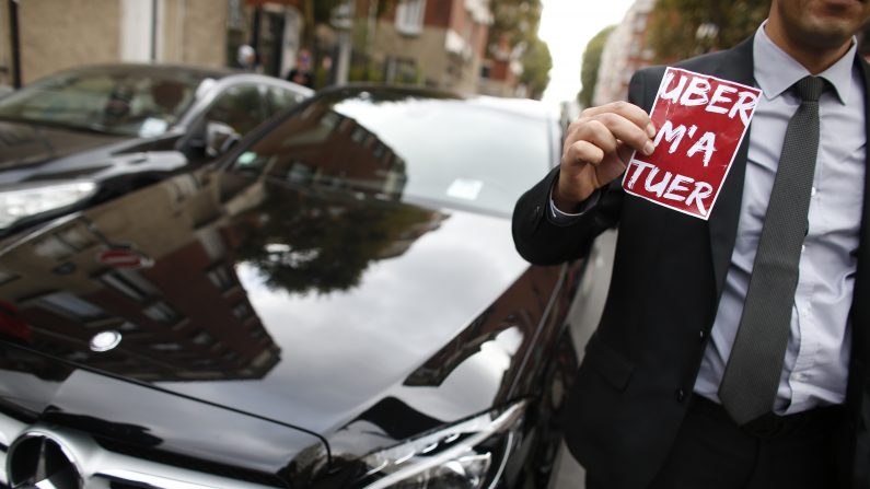 Un conductor que trabaja para la compañía de servicio de alquiler de Uber, conocido como conductores VTC en Francia, muestra una lectura pegatina "Uber me mata", durante una manifestación frente a la sede de la Uber francesa el 13 de octubre, 2015, en París, ya que protestan contra la decisión de Uber de recortar los precios cobrados en París en un 20 por ciento a reunir más precios paseos, pocas semanas después de las compañías Paris Taxis lanzaron una agresiva estrategia de reducción de precios para mantener la cuota de mercado (Photo credit should read THOMAS SAMSON / AFP / Getty Images)