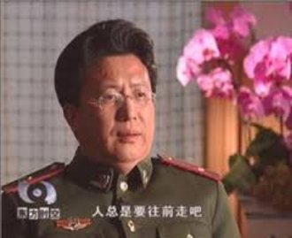 El Dr. Shen Zhongyang en una entrevista con la televisión china, vestido con uniforme paramilitar. El subtítulo dice "la humanidad siempre progresará".
