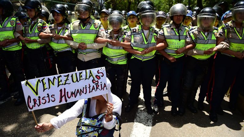 Una manifestante sostiene un cartel que dice 'Venezuela crisis humanitaria SOS', mientras la policía monta guardia en una protesta contra las políticas del gobierno del presidente Nicolas Maduro en Caracas el 26 de mayo de 2016. (RONALDO SCHEMIDT/AFP/Getty Images)