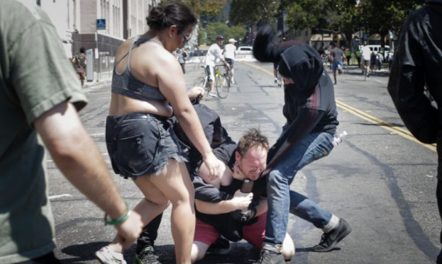 Dos personas vestidas de negro golpean a un hombre acusado de ser un partidario de Trump en MLK Jr. Park en Berkeley, California, el 27 de agosto de 2017. (Elijah Nouvelage / Getty Images)