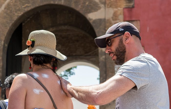 Un hombre pone crema en la espalda de una mujer mientras pasean por los alrededores de la Catedral de Sevilla, hoy que ha comenzado el verano y que, según la aemet, será el menos caluroso de los últimos 4 años. EFE/Raúl Caro.