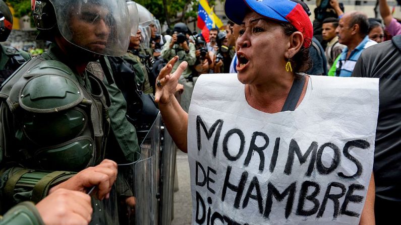 Una mujer con un cartel que dice "Nos morimos de hambre" protesta contra los nuevos poderes de emergencia decretados por el dictador Nicolás Maduro frente a una línea de policías antidisturbios en Caracas el 18 de mayo de 2016.
(FEDERICO PARRA / AFP / Getty Images)