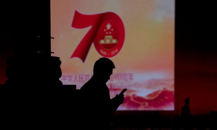 Un hombre usa su teléfono móvil frente a una pantalla que muestra un mensaje sobre el 70º aniversario de la fundación del régimen comunista chino, en Beijing el 26 de septiembre de 2019. (Noel Celis/AFP/Getty Images)