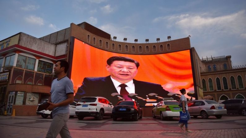 Esta foto, tomada el 4 de junio de 2019, muestra a personas caminando junto a una pantalla que muestra imágenes del líder chino Xi Jinping en Kashgar, en la región occidental de Xinjiang, China. (GREG BAKER/AFP vía Getty Images)