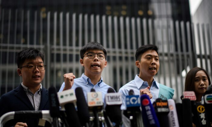 El activista prodemocrático Joshua Wong (2ª iz) y Kelvin Lam (2ª de) gritan consignas mientras se reúnen con los medios de comunicación fuera del Consejo Legislativo (LegCo) en Hong Kong el 29 de octubre de 2019, después de que a Wong le prohibieran presentarse a las próximas elecciones locales. (ANTHONY WALLACE/AFP vía Getty Images)