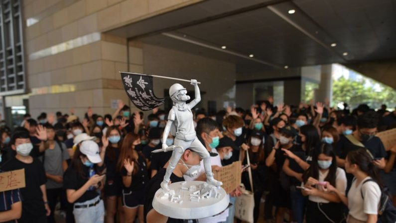 Um homem carrega uma estátua em miniatura enquanto manifestantes e apoiadores se reúnem do lado de fora da entrada do Tribunal de West Kowloon, em Hong Kong, em 2 de outubro de 2019, onde cerca de 96 manifestantes presos e acusados de tumultos durante confrontos com a polícia em 29 de setembro deveriam aparecer em Tribunal. - Comícios espontâneos de multidões eclodiram em Hong Kong em 2 de outubro, quando a raiva aumentou com a polícia disparando contra um manifestante adolescente (Foto por NICOLAS ASFOURI / AFP via Getty Imagens)