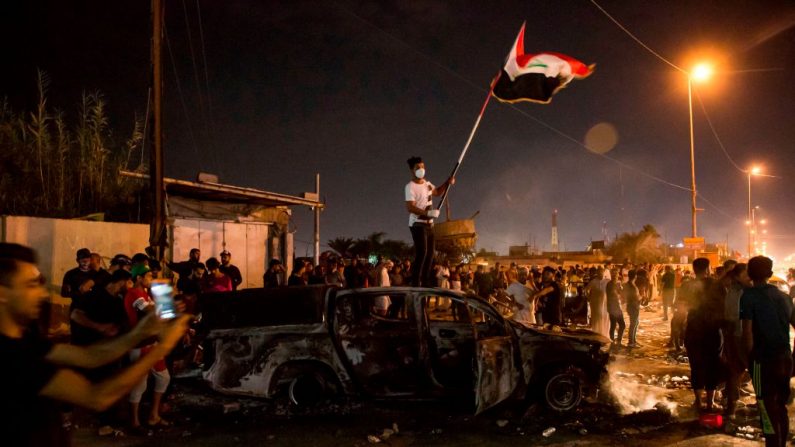Um manifestante iraquiano agita uma bandeira nacional enquanto ele fica no topo de um veículo da polícia incendiado durante uma manifestação antigovernamental fora da sede do governo local na cidade de Basra, no sul, em 25 de outubro de 2019 (Foto: - / AFP via Getty Images)