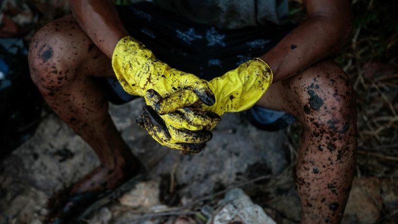 Detalhe das luvas e pernas sujas do óleo cru de um voluntário após a limpeza das algas na praia de Itapuama, no município de Cabo de Santo Agostinho, no estado de Pernambuco, na terça-feira (EFE / Brenda Alcântara)