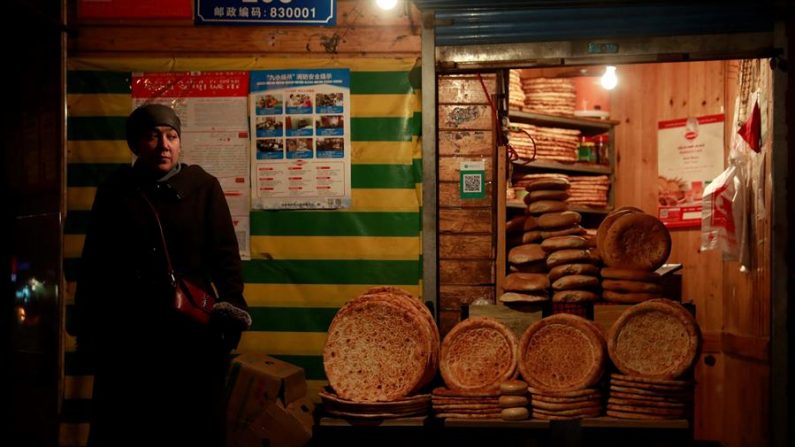 Una mujer de etnia uigur junto a una tienda que vende pan en la ciudad de Urumqi, provincia autónoma uigur de Xinjiang, China. EPA/HOW HWEE YOUNG/Archivo