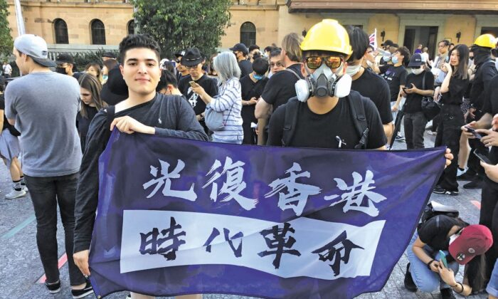 Drew Pavlou (Izq.), en una protesta con una pancarta que dice "Liberen a Hong Kong, la revolución de nuestro tiempo". (Cortesía de Drew Pavlou)