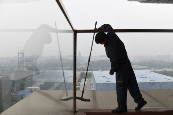 Trabalhador limpa as janelas do terraço de um hotel em frente ao Parque Florestal Olímpico (atrás), construído para os Jogos Olímpicos de Pequim em 2008, em um dia poluído em Pequim em 21 de junho de 2019 (NICOLAS ASFOURI / AFP via Getty Images)