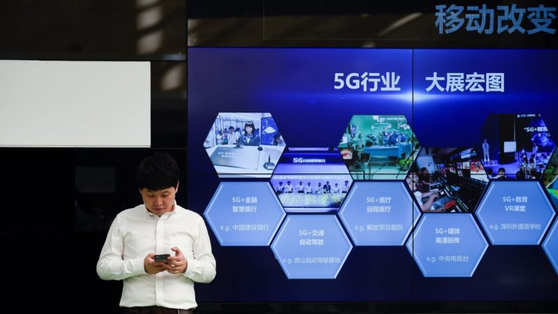Un hombre usa su teléfono móvil frente a una pantalla que muestra la industria 5G de China fuera de una oficina de telecomunicaciones en Beijing el 25 de septiembre de 2019. (WANG ZHAO/AFP vía Getty Images)