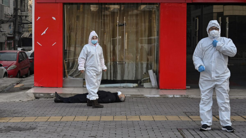 Funcionarios chinos con trajes protectores que controlan a un anciano con una máscara facial que se derrumbó y murió en una calle cerca de un hospital en Wuhan, China, el 30 de enero de 2020. (HECTOR RETAMAL / AFP a través de Getty Images)