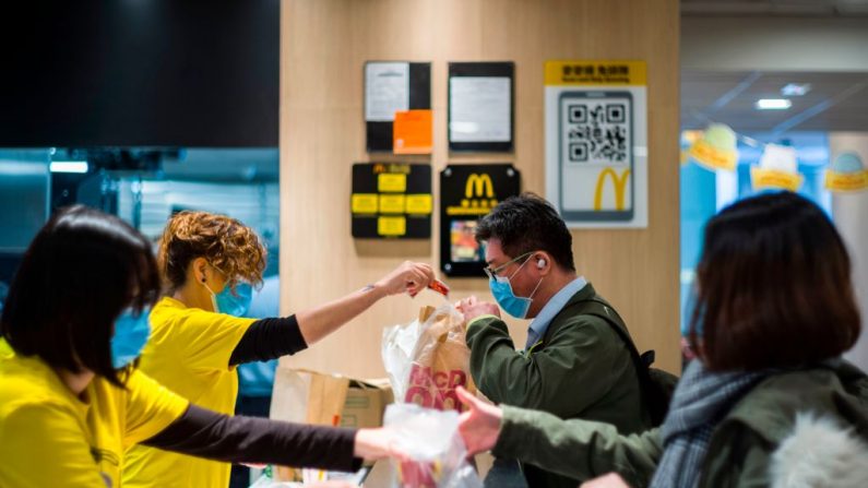 Personal de la reconocida cadena (izq.) y clientes (der.) llevan barbijos en el mostrador de un restaurante de comida rápida de MacDonald's en Hong Kong, el 29 de enero de 2020, como medida preventiva tras un brote de coronavirus que comenzó en la ciudad china de Wuhan.  (Foto de Anthony WALLACE / AFP) (Foto de ANTHONY WALLACE/AFP vía Getty Images)