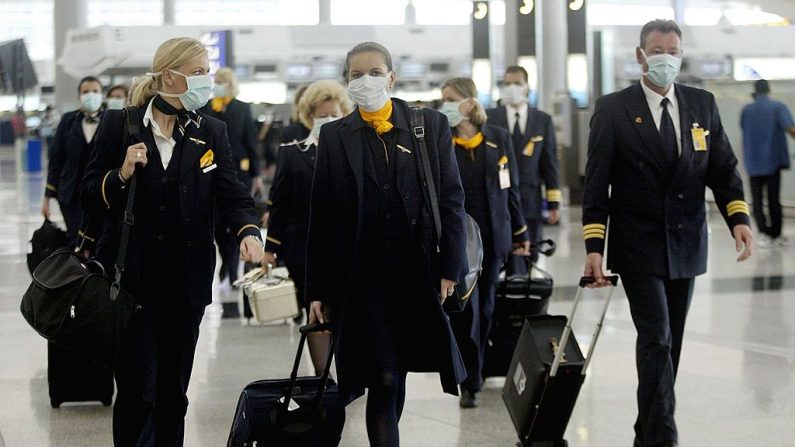 Tripulación de la compañía alemana Lufthansa camina por el Chek Lap Kok de Hong Kong con máscaras para protegerse contra un brote mortal de neumonía 14 de abril de 2003. La principal compañía aérea del territorio, Cathay Pacific, dijo que no descartaba la posibilidad de que su flota de pasajeros se quedara en tierra, ya que la demanda de viajes de entrada y salida de Hong Kong ha sido devastada por el brote de la enfermedad conocida como Síndrome Respiratorio Agudo Severo (SARS). (PETER PARKS/AFP/GettyImages)

