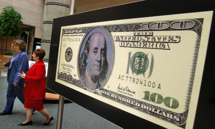 Dos mujeres no identificadas pasan junto a un billete de 100 dólares en un vídeo durante una visita a la exposición "Dinero en movimiento" en el Banco de la Reserva Federal de Filadelfia en Filadelfia, Pensilvania, el 2 de julio de 2003. (William Thomas Cain/Getty Images)