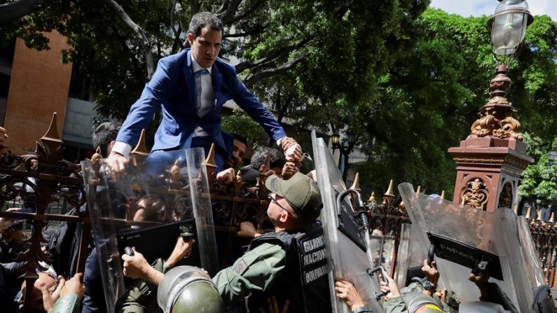 Juan Guaidó trepa una reja en un intento por ingresar a la sede de la Asamblea Nacional, custodiada por la policía para impedir su ingreso y el de diputados opositores este domingo, en Caracas (Venezuela). (EFE/ Rayner Peña)
