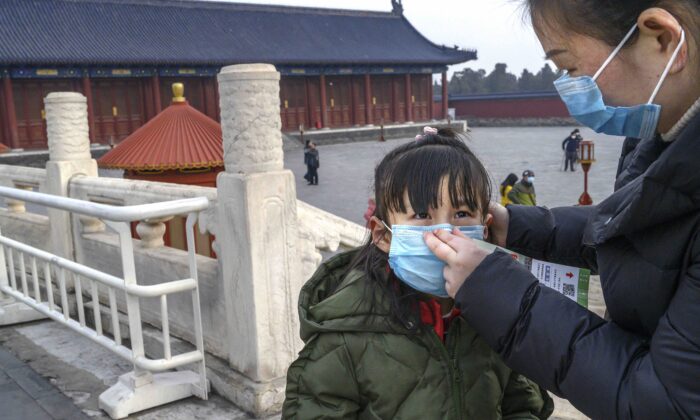 Una mujer china le pone una máscara protectora a una niña en el Templo del Cielo, en Beijing, China, el 27 de enero de 2020. (Kevin Frayer/Getty Imágenes) 