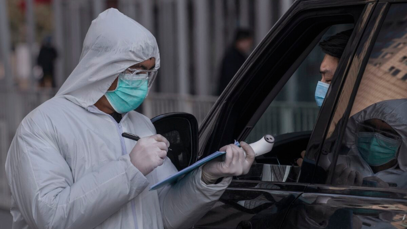 Un trabajador chino usa un traje de protección mientras toma el nombre de un conductor en un vehículo que ingresa a un edificio de oficinas mientras revisa a las personas en Beijing el 10 de febrero de 2020. (Kevin Frayer / Getty Images)