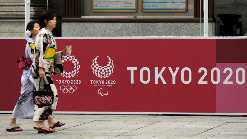 Peatones caminan delante de un tablero que muestra los logotipos de Tokio 2020 para los próximos Juegos Olímpicos. (KAZUHIRO NOGI/AFP vía Getty Images)