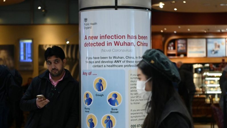 Una mujer con una máscara facial pasa un cartel de Salud Pública de Inglaterra, advirtiendo a los pasajeros que llegan que se ha detectado un virus, el Coronavirus, en Wuhan en China, en la Terminal 4 del Aeropuerto Heathrow de Londres. (Foto de DANIEL LEAL-OLIVAS / AFP) (Foto de DANIEL LEAL-OLIVAS/AFP vía Getty Images)
