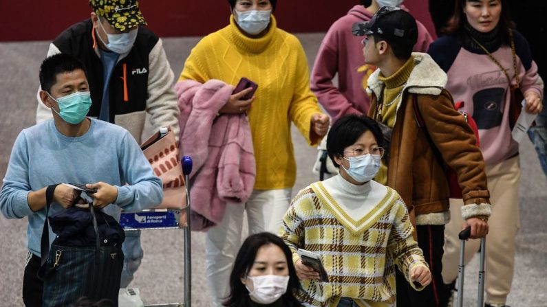 Los pasajeros que usan máscaras respiratorias caminan a través de una terminal hacia el mostrador de facturación el 31 de enero de 2020 en el aeropuerto Fiumicino de Roma, Italia. (TIZIANA FABI/AFP/Getty Images)