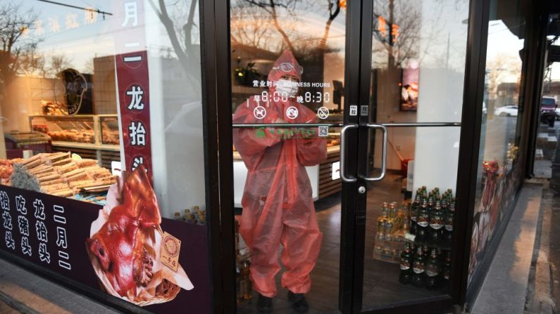 Una trabajadora usa un traje protector y una máscara facial mientras se encuentra en la entrada de una tienda en Beijing el 17 de febrero de 2020. - La cifra de muertos por la epidemia de coronavirus COVID-19 de China aumentó, dijo la Comisión Nacional de Salud el 17 de febrero. (GREG BAKER / AFP a través de Getty Images)