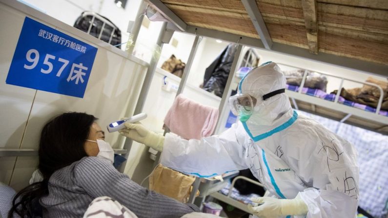 Esta foto tomada el 17 de febrero de 2020 muestra a un miembro del personal médico comprobando la temperatura corporal de una paciente que ha mostrado síntomas leves del coronavirus COVID-19, en un centro de exposiciones convertido en un hospital en Wuhan, en la provincia central de Hubei en China. (Foto de STR/AFP vía Getty Images)