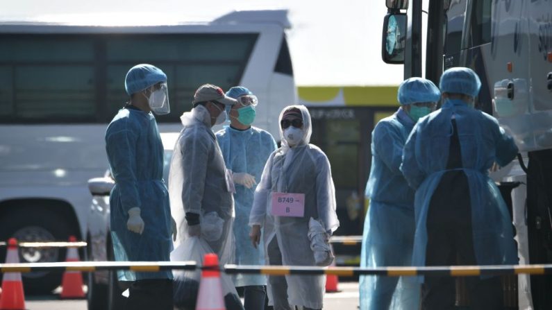 Trabajadores con ropa protectora ayudan a los pasajeros a subir a un autobús después de desembarcar del crucero Diamond Princess, en cuarentena por temor al nuevo coronavirus COVID-19, en la terminal de cruceros del muelle Daikoku en Yokohama, Japón, el 21 de febrero de 2020. (PHILIP FONG / AFP / Getty Images)