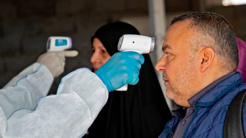 Un miembro de un equipo médico toma la temperatura de los viajeros iraquíes en el cruce fronterizo de Shalamjah, a unos 15 kilómetros al sureste de la ciudad de Basora, a su regreso de Irán el 21 de febrero de 2020. (HUSSEIN FALEH / AFP / Getty Images)