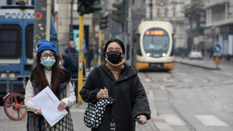 Dos mujeres jóvenes, ambas con máscara respiratoria, caminan por las calles el 25 de febrero de 2020 en Milán, Italia. (Emanuele Cremaschi/Getty Images)