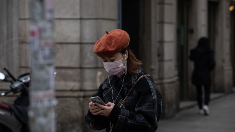 Una mujer, con una máscara respiratoria, usa su smartphone mientras está de pie en el distrito Paolo Sarpi (el barrio chino de Milán) el 25 de febrero de 2020 en Milán, Italia. (Emanuele Cremaschi/Getty Images)