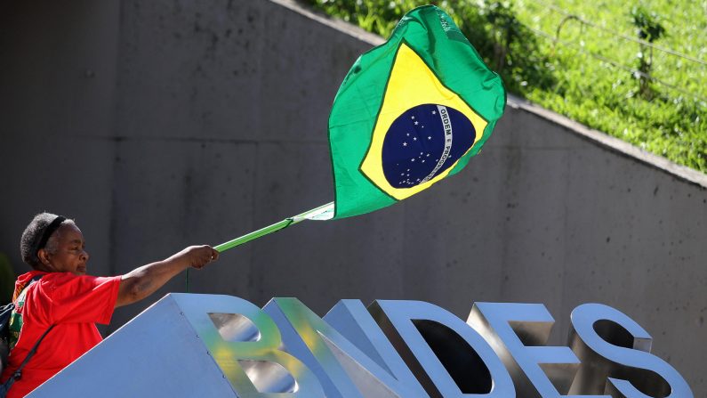 Una mujer mayor ondea una bandera brasileña sobre el logotipo del Banco Nacional de Desarrollo de Brasil (BNDES) durante una manifestación de trabajadores del sector petrolero contra la Comisión Parlamentaria de Investigación (CPI) creada por el congreso para investigar las acusaciones de corrupción que involucran a la empresa estatal brasileña de petróleo Petrobras, en Río de Janeiro el 21 de mayo de 2009. (VANDERLEI ALMEIDA/AFP a través de Getty Images)