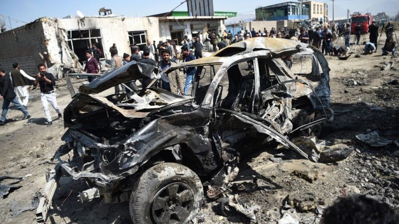 Personal de seguridad y civiles afganos se reúnen junto a un coche dañado en el lugar de un atentado con coche bomba en Kabul el 17 de marzo de 2018. Un atacante suicida talibán hizo estallar un coche cargado de bombas en Kabul durante la hora punta el 17 de marzo, matando al menos a dos civiles, mientras los militantes aumentan la presión en la capital en medio de los llamamientos a las conversaciones de paz. (WAKIL KOHSAR/AFP a través de Getty Images)