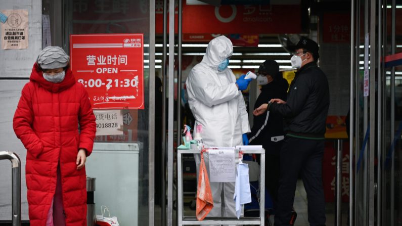 Un empleado de un supermercado que lleva un traje de protección utiliza un termómetro para comprobar la temperatura de la entrada de un supermercado en Beijing el 29 de febrero de 2020. (STR/AFP vía Getty Images)