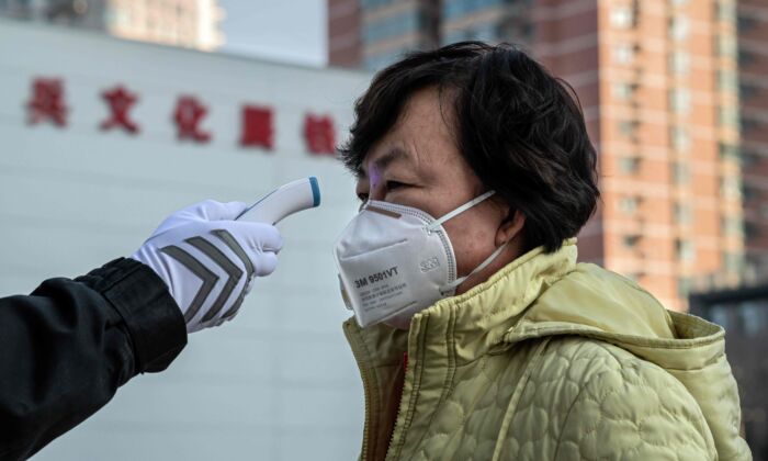 Un guardia de seguridad verifica la temperatura de una mujer con una máscara protectora en la entrada de un parque en Beijing, China, el 31 de enero de 2020. (NICOLAS ASFOURI / AFP a través de Getty Images)