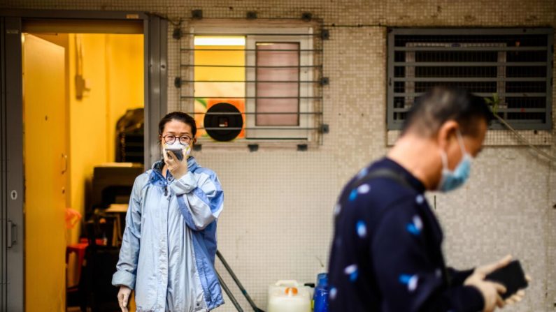 Una mujer con una mascarilla usa su teléfono junto a contenedores de peróxido de hidrógeno en Hong Kong el 11 de febrero de 2020. (Anthony Wallace/AFP vía Getty Images)