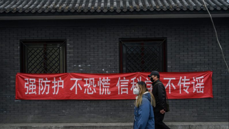 Un hombre y una mujer chinos usan máscaras protectoras cuando pasan una pancarta que dice "prevención fuerte, no se asuste, crea en la ciencia, no difunda rumores" en una pared en un área residencial en Beijing, China, el 20 de febrero, 2020. (Kevin Frayer/Getty Images)
