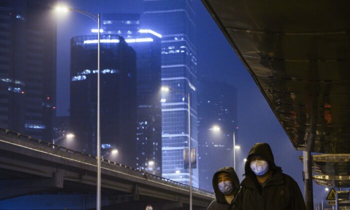 Ciudadanos chinos usan máscaras protectoras y miran sus teléfonos móviles mientras esperan al autobús en una calle casi vacía del normalmente concurrido Distrito Central de Negocios durante la hora punta del viernes en Beijing, China, el 7 de febrero de 2020. (Kevin Frayer/Getty Images)