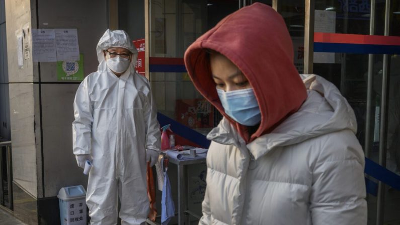 Un trabajador chino lleva un traje protector y una máscara mientras espera para comprobar la temperatura de los clientes que entran en una tienda de comestibles en Beijing, China, el 28 de febrero de 2020. (Kevin Frayer/Getty Images)