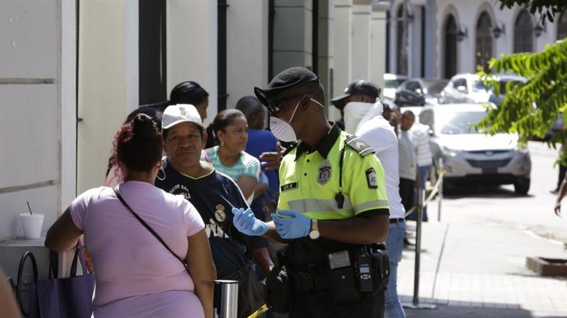 Un policía controla la fila de decenas de personas para comprar billetes de lotería, acción que desafía las medidas de seguridad y no aglomeración, este lunes, en Ciudad de Panamá (Panamá). EFE/Carlos Lemos
