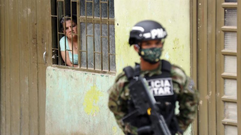 Una mujer observa este lunes a un efectivo de la Policía Militar que utiliza tapabocas, mientras soldados de la Brigada 13 del Ejército Nacional de Colombia distribuyen ayuda a personas de bajos ingresos económicos, en el municipio de Soacha (Colombia). EFE/Mauricio Dueñas Castañeda
