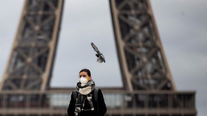 Una mujer con máscara protectora camina junto a la Torre Eiffel, en París, Francia, el 14 de marzo del 2020. El primer ministro francés, Édouard Philippe, ordenó este sábado el cierre a partir de la medianoche de todos los establecimientos abiertos al público "no indispensables" ante una aceleración de la difusión del COVID-19 en las últimas horas que atribuyó a que no se respetan las consignas oficiales. (EFE/Ian Langsdon)