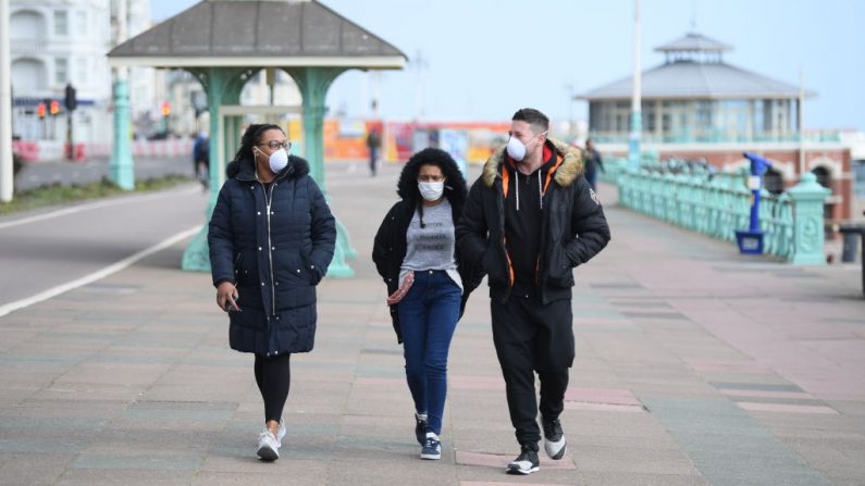 Personas con máscaras faciales caminan por el paseo marítimo el 28 de marzo de 2020 en Brighton, Inglaterra. (Mike Hewitt/Getty Images)