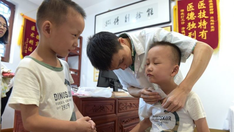 Un niño recibe sanfutie, vendas terapéuticas llenas de hierbas medicinales colocadas en puntos de acupuntura, en el cuello en un hospital de medicina tradicional china el 17 de julio de 2018 en Yiwu, provincia de Zhejiang de China. (Foto de VCG / Getty Images)