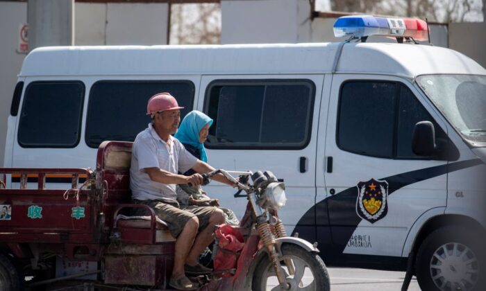 Los musulmanes locales pasan un automóvil policial con su motocicleta en Hotan, en la Región Autónoma Uigur de Xinjiang de China, el 23 de junio de 2017. (Johannes Eisele/AFP a través de Getty Images)