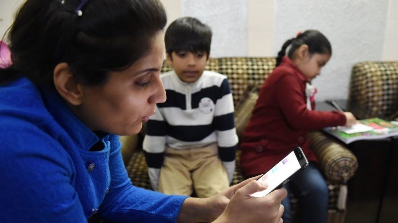 Imagen ilustrativa de una mujer usando un teléfono celular en compañía de niños. (Foto de MONEY SHARMA/AFP vía Getty Images)