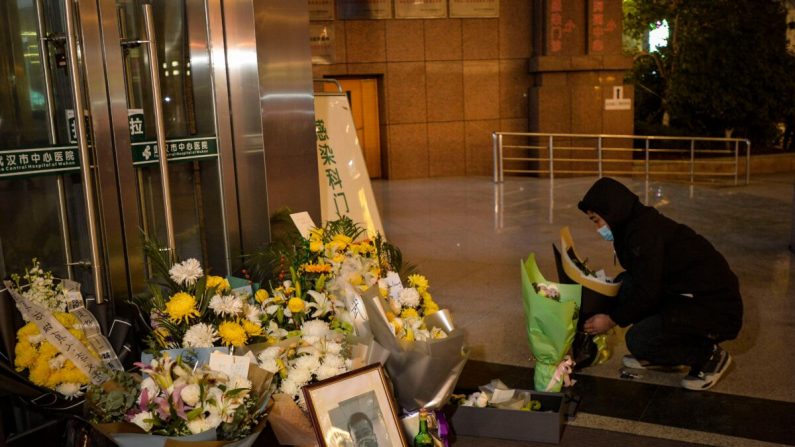 Un hombre está colocando flores junto a una foto del difunto oftalmólogo Li Wenliang afuera del Hospital Central de Wuhan en Wuhan, China, el 7 de febrero de 2020. (STR/AFP a través de Getty Images)