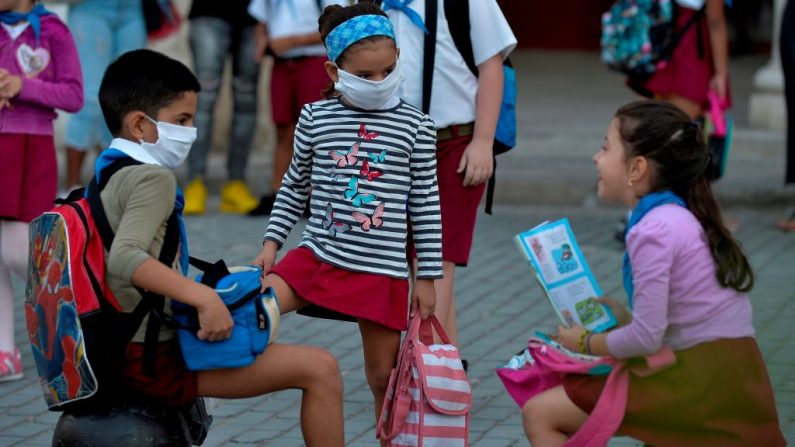 Los alumnos, algunos con máscaras faciales como medida preventiva contra el virus del PCCh, charlan antes de llegar a la escuela en La Habana, Cuba, el 16 de marzo de 2020. (YAMIL LAGE/AFP vía Getty Images)